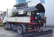 Emulsion spraying machine rested on truck body, with hydraulic bar.